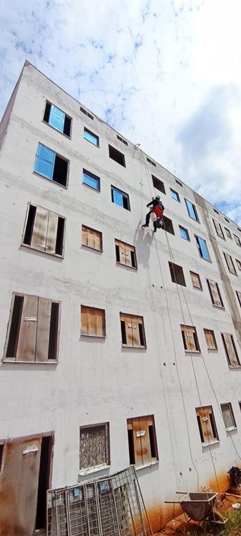 Profissional instalando tubulação em fachada de prédio com acesso por corda